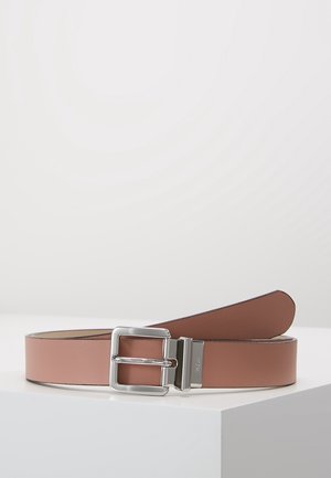 Ceinture en cuir marron avec une boucle rectangulaire argentée, placée enroulée sur une surface blanche sur un fond gris clair.