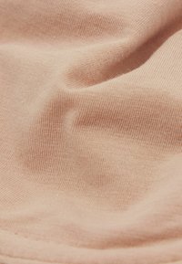 Světlý broskvový materiál s jemnou texturou a tenkým žebrovaným vzorem, s mírnými záhyby a zakřiveními, které zdůrazňují jeho hladký vzhled.