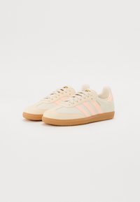 Baskets en daim beige avec des accents rose clair, dotées d'un design à trois bandes, d'une semelle extérieure en caoutchouc naturel et d'une fermeture à lacets.