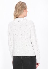 White sweater with speckled black accents, featuring a round neck and ribbed hem, displayed from the back on a model wearing a black skirt.