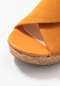 Sandalo in suede arancione con design a fasce incrociate, soletta in pelle arancione liscia e una piattaforma chunky in sughero.