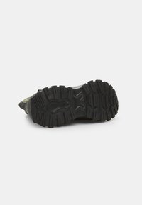 Suela de goma negra con ranuras profundas y estrías para tracción. Bordes reforzados y diseño robusto para durabilidad. En general, apariencia robusta.