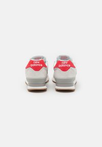 White and grey sneakers with a red heel tab, featuring "new balance" branding. Textured suede and rubber sole have light brown accents.