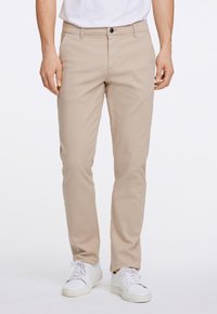 Beige chino's met een rechte pijp, uitgerust met een rits en knoopsluiting, en voorzakken. Gepaard met witte sneakers.