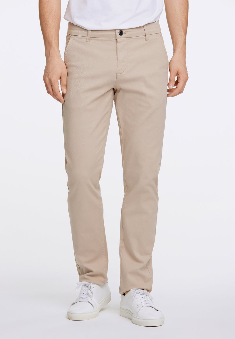 Beige chino's met een rechte pijp, uitgerust met een rits en knoopsluiting, en voorzakken. Gepaard met witte sneakers.