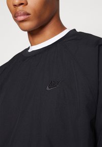 Black Nike sweatshirt with a round neck, featuring a white inner collar. The design includes a small embroidered logo on the chest.