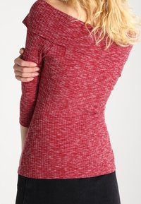 Top rosso, testurizzato, con design off-the-shoulder e maniche a tre quarti. Il tessuto presenta un delicato motivo mélange.