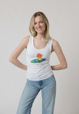 Junge Frau mit blondem Haar lächelt, trägt ein weißes Tanktop mit Cartoon-Surfer und blaue Jeans, steht mit den Händen hinter dem Rücken.