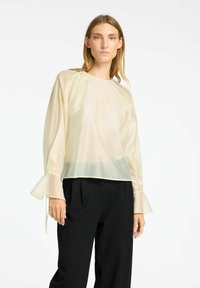 Blusa leggera in crema trasparente con una vestibilità comoda, scollatura rotonda e maniche a campana, abbinata a pantaloni neri su misura.