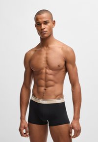 Boxer-briefs noirs avec une ceinture élastique beige portant le nom de la marque "BOSS" dans une teinte plus claire. Tissu lisse, design ajusté.