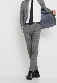 Szary garnitur w kratę o dopasowanym kroju, jednorzędowa marynarka i pasujące spodnie; posiada kontrastową niebieską podszewkę w wzory.