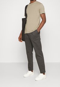 Herrtröja i olivgrön färg med korta ärmar, i kombination med mörkgrå tapered-byxor och vita sneakers. Enkelt, avslappnat design.