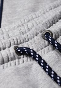 Grijze stof met een trekkoord met een blauw-wit patroon, elastische taille en metalen hardware met merkdetails.