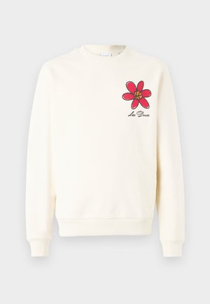 Sweatshirt crème avec un motif de fleur rouge au centre jaune et contours noirs. Manches et ourlet côtelés. Texture de tissu douce.