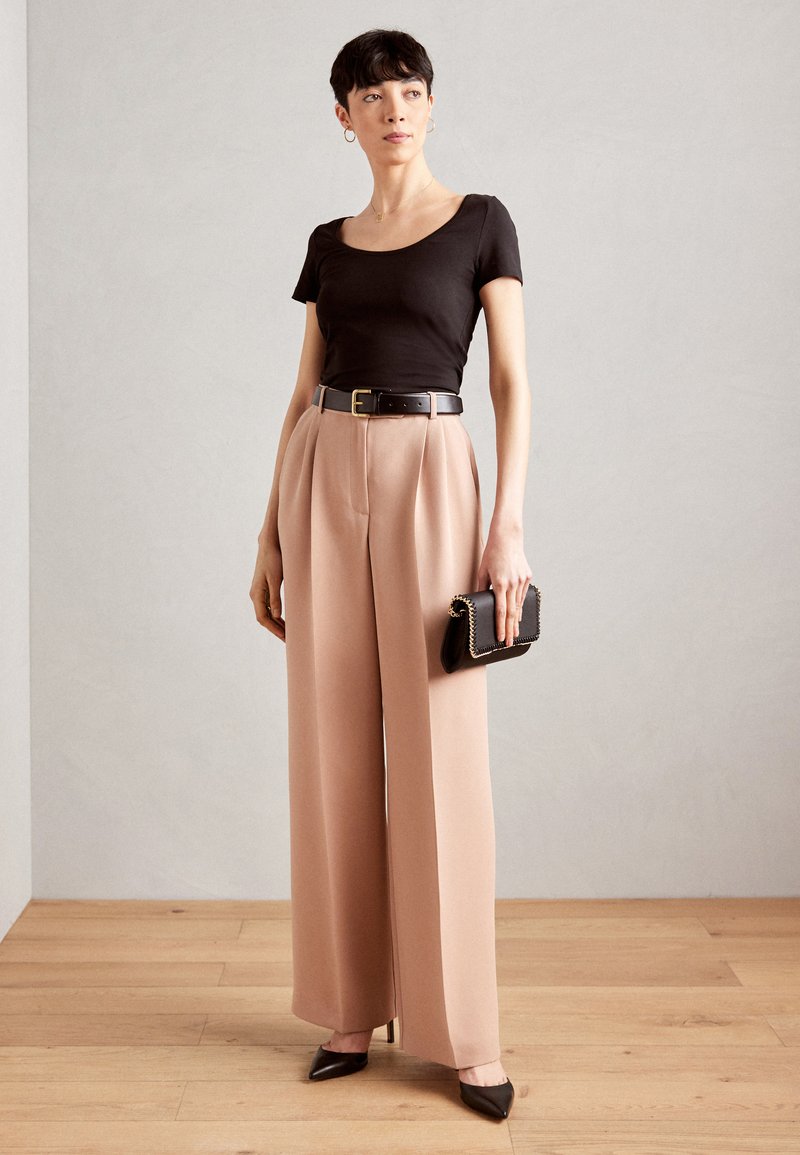 Sort tætsiddende t-shirt, høj talje lyserøde brede bukser, sort bælte og clutch. Spidse sorte hæle fuldender outfittet.