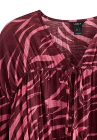 Viininpunainen paita, jossa on vaaleanpunaisia, aaltoilevia raitoja. Ominaisuuksiin kuuluvat V-pääntie, solmityksellinen yksityiskohta edessä ja virtaava kangas, jossa on kevyitä ominaisuuksia.