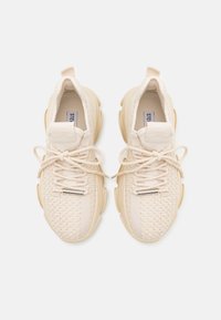 Paire de baskets beiges tricotées avec semelles épaisses, fermeture à lacets et languettes en tissu, vues de dessus sur un fond uni.