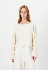 Cream cropped sweater with a wide boat neckline, long sleeves, and raw hems, paired with a matching soft, flowy bottom. Smooth texture.