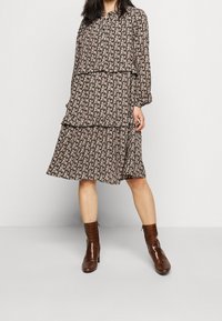 Svart blommig klänning med lagerdesign, långa ärmar, knappstängning och en fladdrande silhuett. Matchad med bruna ankelskoot.