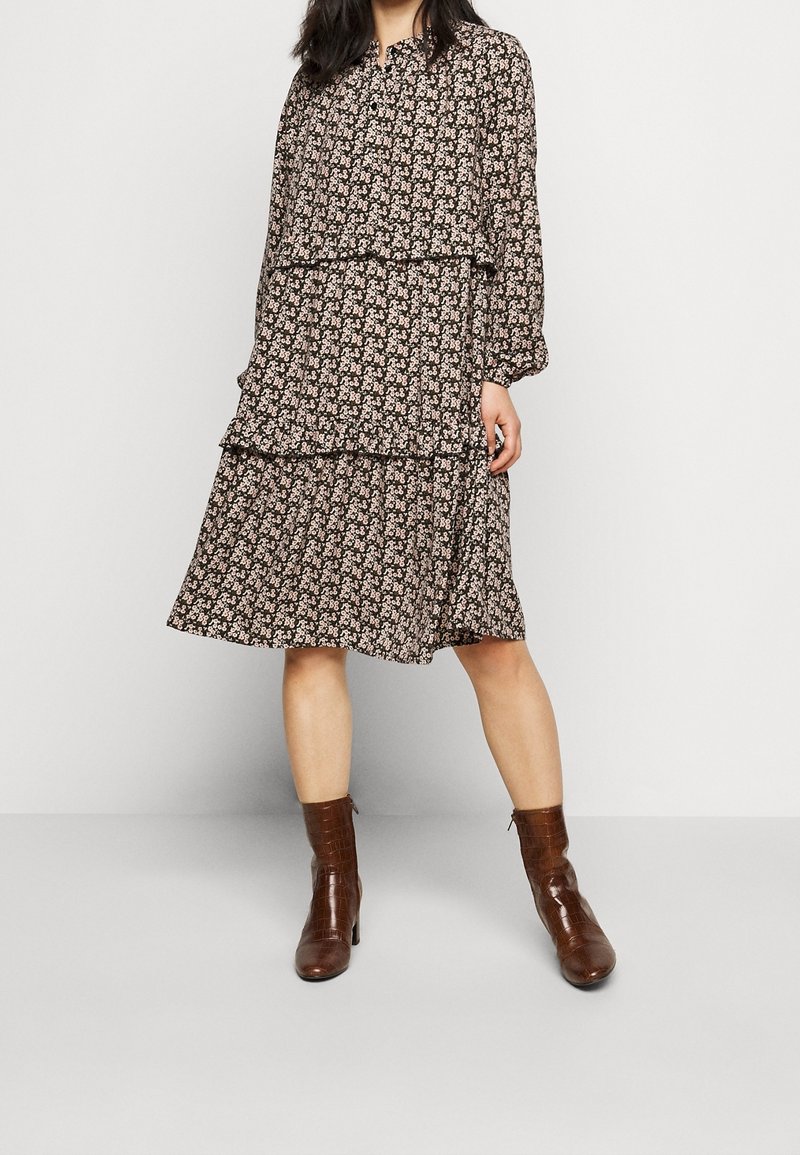 Svart blommig klänning med lagerdesign, långa ärmar, knappstängning och en fladdrande silhuett. Matchad med bruna ankelskoot.