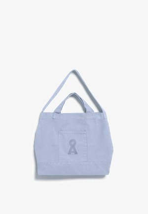 Sac cabas en toile bleu clair avec anses courtes et longues, poche avant et logo brodé en forme de serrure sur fond blanc.