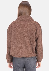 Braune, flauschige, übergroße Jacke mit Kragen und langen Ärmeln, die aus einem strukturierten Stoff besteht. Die Rückansicht zeigt eine lockere Passform und einen abgerundeten Saum.