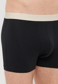 Črne bokserice iz mehkega blaga, z bež elastičnim pasom in ravnimi šivi za udobje.