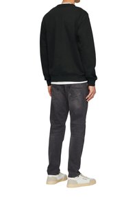 Zwarte sweatshirt met geribbelde manchetten, gecombineerd met donkergrijze jeans. Witte shirt eronder en grijs-witte sneakers. Casual fit.
