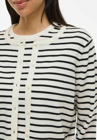 Cardigan a righe con strisce nere orizzontali su fondo crema, scollatura rotonda e chiusura con bottoni sul davanti.