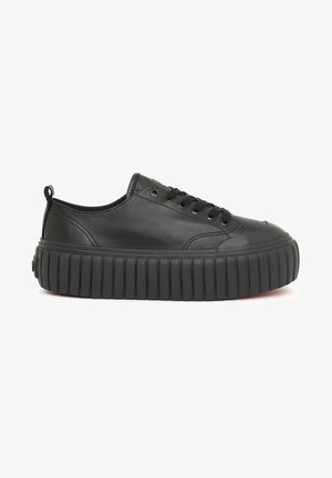 Zapatilla de cuero negro con punta redondeada, cordones planos y una suela gruesa y estriada. Cuenta con una pestaña en la parte posterior para facilitar su uso.