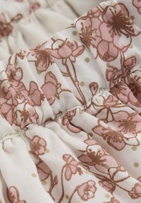 Tissu floral avec des fleurs roses et brunes sur un fond crème, présentant une texture froncée et de subtils pois verts.