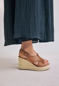 Sandale compensée en cuir marron clair avec brides croisées et boucle, dotée d'une plateforme espadrille texturée et d'un bout ouvert.