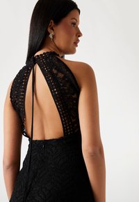 Black lace halter dress featuring a high neckline and an open back design. Detailed with geometric patterns and a fitted silhouette.