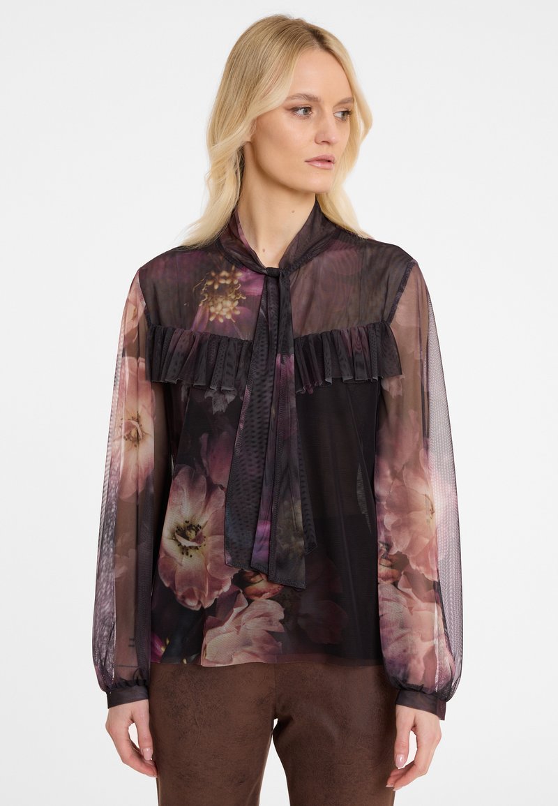 Durchsichtige schwarze Bluse mit floralem Muster, gerafftem Dekolleté und Krawattenkragen. Lange durchsichtige Ärmel mit eng anliegenden Manschetten.
