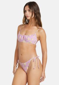 Floral bikini set in light pink with thin straps, ruffled detailing on the top, and adjustable side ties on the bottom. Soft, textured fabric.