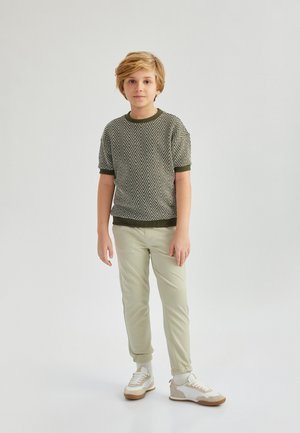 Groene textuur korte mouwen trui met visgraatpatroon, gecombineerd met lichtgroene taps toegesneden broek en crèmekleurige sneakers met beige accenten.