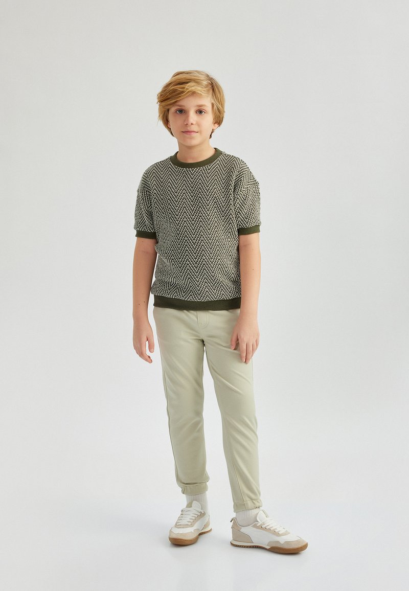 Suéter corto de manga corta texturizado en verde con patrón de espiga, combinado con pantalones tapered verdes claros y zapatillas crema con acentos beis.