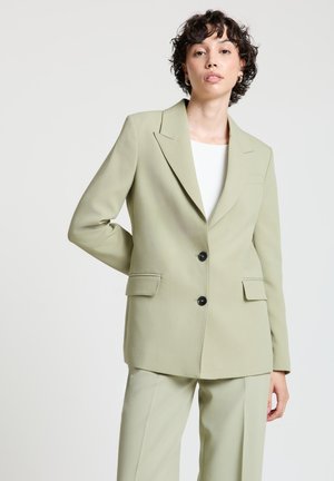 Blazer vert clair cintré avec un col cranté, deux poches avant et des boutons noirs ; texture lisse et coupe structurée.