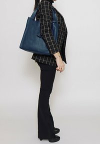 Borsa tote in pelle blu con finitura testurizzata e doppio manico per spalla, caratterizzata da un design minimalista e forma angolare.