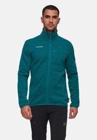 Giacca in fleece verde acquamarina con colletto alto, zip completa e tasche con zip. Presenta un tessuto testurizzato e un logo del marchio ricamato sul petto.