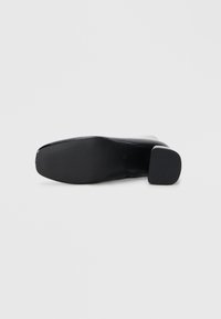 Schwarze Stiefelette mit einem Obermaterial aus glattem Leder, quadrater Zehenform und breitem Blockabsatz. Die Sohle hat horizontale Rillen für besseren Grip.
