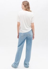 Weißes T-Shirt mit kurzen Ärmeln, kombiniert mit hellblauen, weit geschnittenen Jeans, die ein schlichtes Design und einen weichen Stoff mit Gesäßtaschen aufweisen.