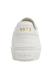 White leather sneaker featuring a textured back, gold "1973" lettering, and a rubber sole with a logo patch at the heel.