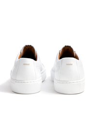 Witte leren sneakers met eenvoudig ontwerp, afgeronde vorm, gestructureerde rubberen zool en subtiele stiksels. Bruine binnenvoering zichtbaar.