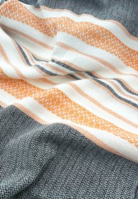 Geweven textiel met zwarte, witte en oranje strepen. Genopte oppervlakte met een mix van kleuren en patronen, wat een dynamisch ontwerp creëert.