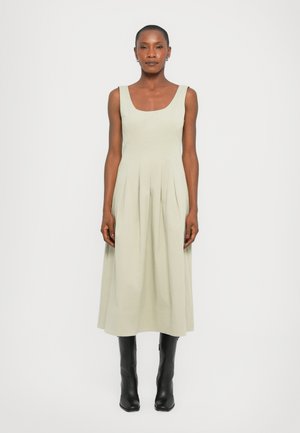 Light green sleeveless dress with a square neckline, pleated skirt detail, and mid-calf length, paired with black knee-high boots.