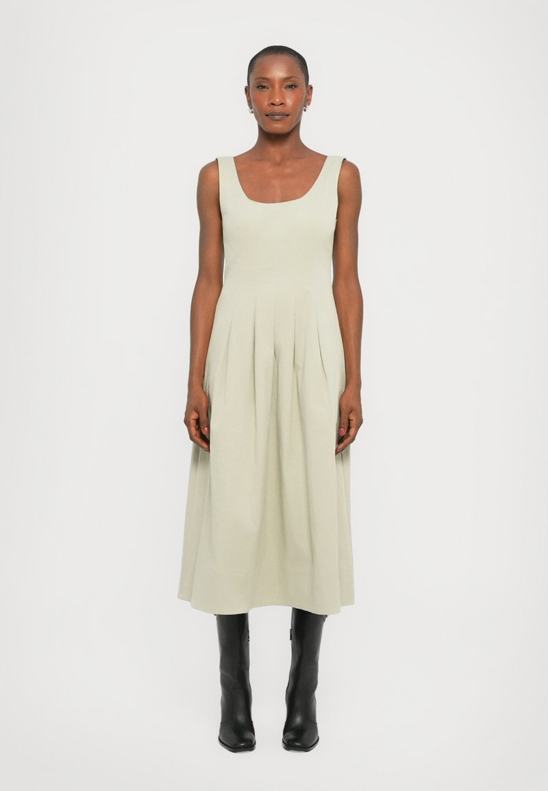 Light green sleeveless dress with a square neckline, pleated skirt detail, and mid-calf length, paired with black knee-high boots.