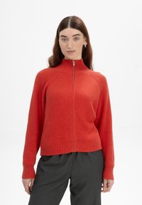 Rode geribde rits trui met hoge kraag en lange mouwen, met een textuur stof en een aansluitende pasvorm. Gecombineerd met grijze broeken.