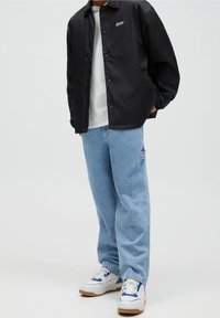 Czarna kurtka z zapięciem na napy, biała koszulka, jasnoniebieskie luźne dżinsy i białe sneakersy z niebieskimi i żółtymi akcentami. Gładki materiał, casualowy krój.