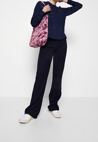 Camicia blu navy con bottoni e dettagli in pizzo, abbinata a pantaloni larghi scuri e sneakers bianche con dettagli gialli. Borsa a mano rosa floreale.